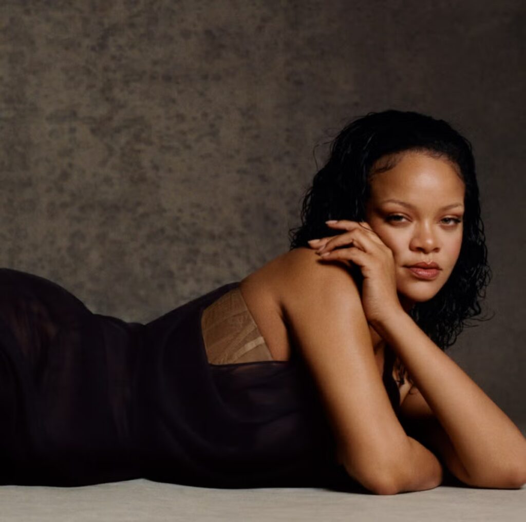 Rihanna lying on the ground against a dark background, creating a bold and magnetic atmosphere in a portrait often associated with her powerful public image.