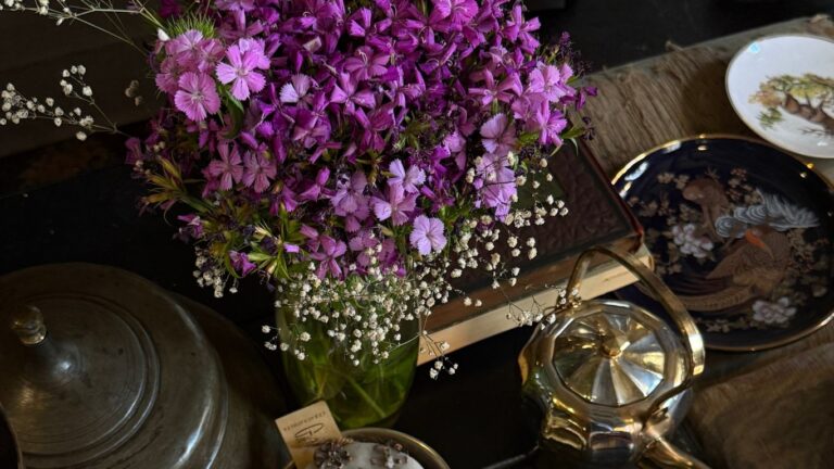Venus in Cancer mood: a bouquet of purple and white flowers on a vintage table with books, porcelain dishes, and a silver teapot.