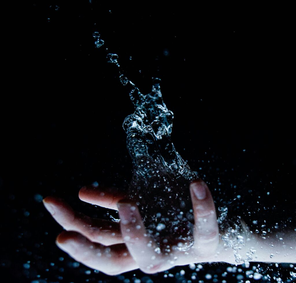 Pisces Season 2026 symbolic image of a hand releasing splashing water in the dark, representing emotional flow.