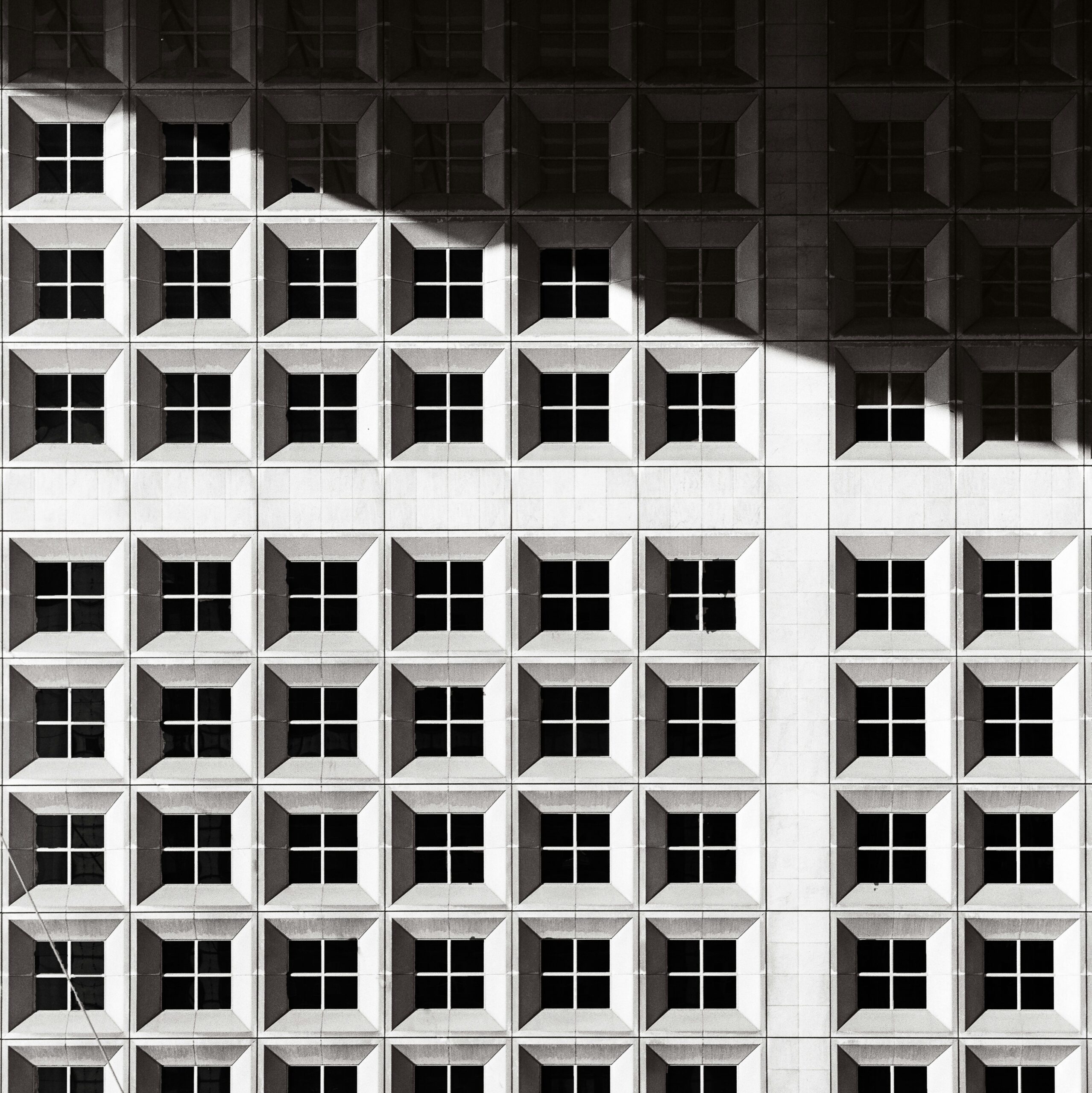 Grand Cross aspect in astrology represented by a black and white photograph of a building façade with a geometric pattern and a strong, dramatic shadow.
