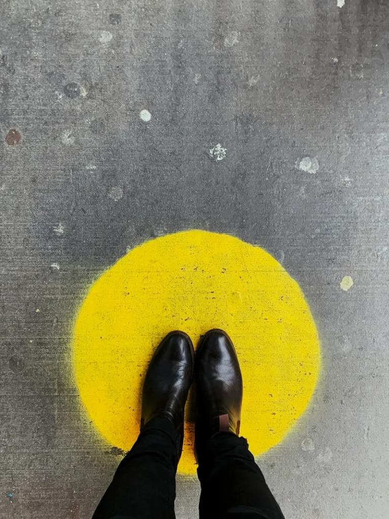 Gemini season symbolic image of two feet seen from above standing on a yellow circle, representing choice, direction, and focused attention within movement.