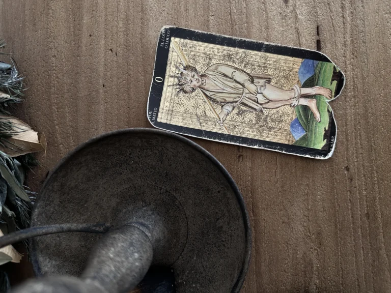 Vintage Fool tarot card from the Visconti Sforza deck on a wooden surface.