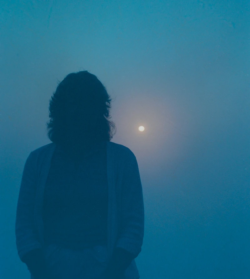 Man seen from behind looking at the moon in an intense blue, misty atmosphere, evoking introspection, mystery, and subtle mental shifts linked to the New Moon in Gemini