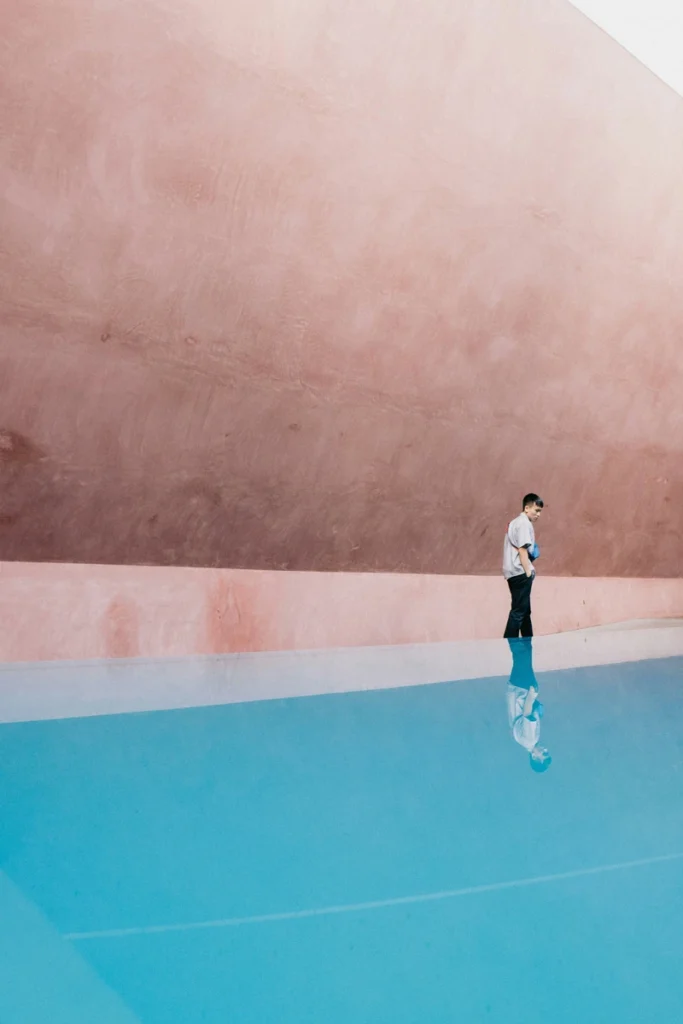 sagittarius rising street photography with a person walking across a blue pavement and pink wall background, vibrant movement and playful expansive atmosphere