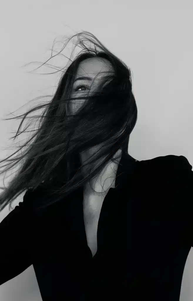 scorpio rising black and white portrait of a woman with hair covering her face in the wind, expressing mystery, emotional intensity, and hidden identity