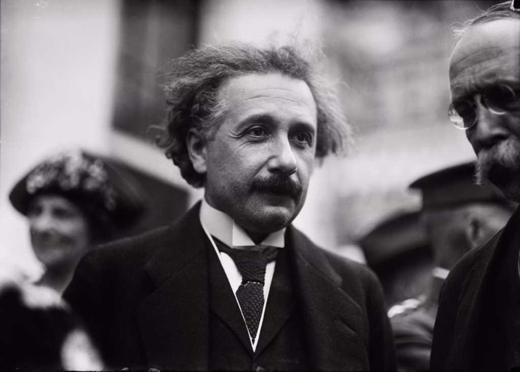 Albert Einstein's black and white portrait of him wearing a suit in the middle of other people.