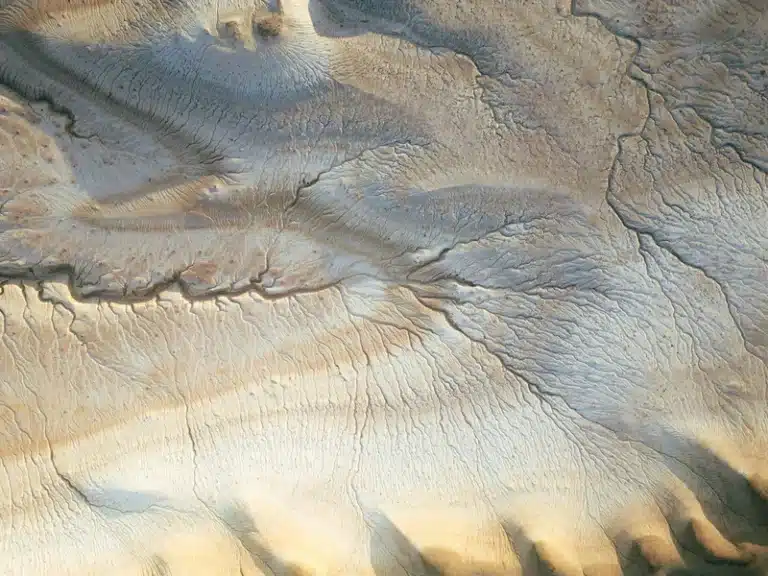 Virgo New Moon reflected in an aerial view of a textured desert landscape in soft beige and blue-grey tones, evoking grounded Earth energy.