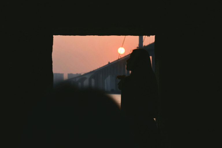 Libra Season meaning captured by the silhouette of a woman watching the sunset beside a bridge, symbolising balance between light and shadow.