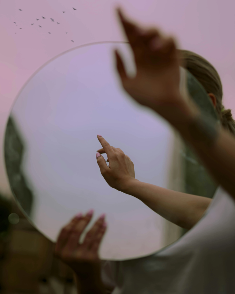 Mirror of the Soul – Astrology and Self-Awareness Mirror in pink and purple tones reflecting a pair of hands, evoking self-awareness, introspection, and the birth chart as a mirror of the soul.