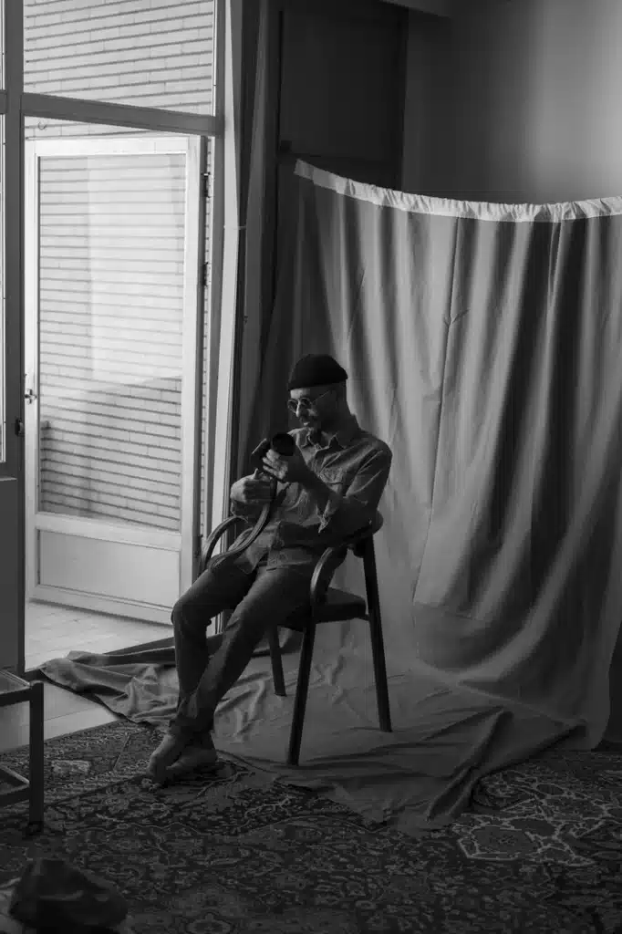 Black-and-white photograph of a young man sitting beside a window with a camera, reflecting the connection between astrology, self-awareness, and the birth chart as a mirror of the soul.