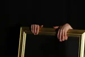 Libra New Moon image with hands holding a golden mirror against a dark background, symbolizing reflection, balance, beauty, and inner awareness.