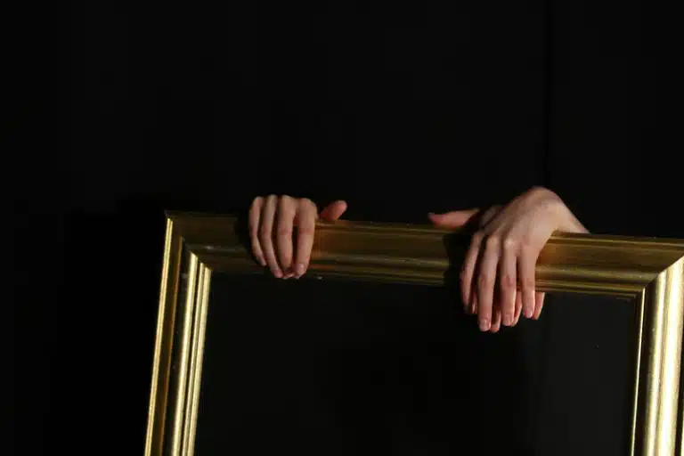 Libra New Moon image with hands holding a golden mirror against a dark background, symbolizing reflection, balance, beauty, and inner awareness.