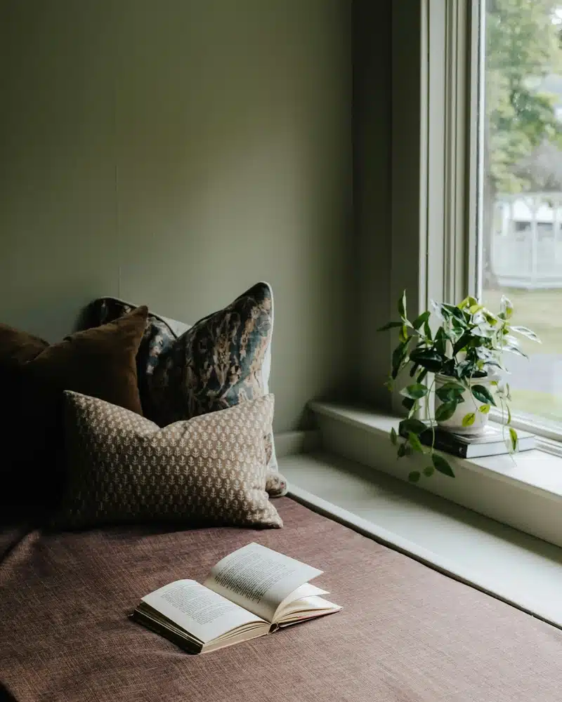 New Moon in Libra image with a quiet reading nook by a window, soft pillows, an open book, and a plant, evoking balance, reflection, and peaceful new beginnings.