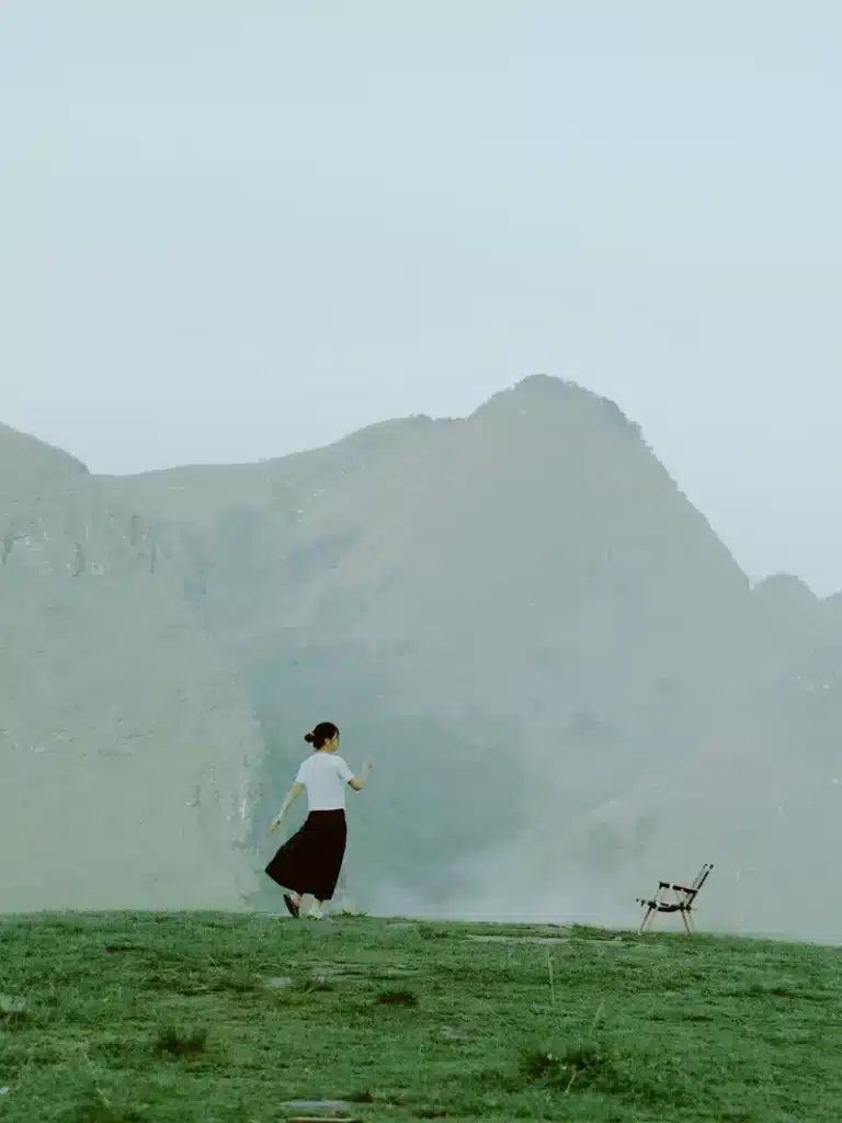 Saturn in Gemini traits symbolized by a solitary woman walking through a misty mountain landscape beside an empty chair.