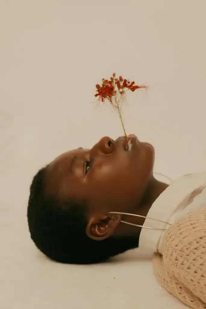A person rests with a small red flower between their lips, evoking the introspective mood of the New Moon in Scorpio.