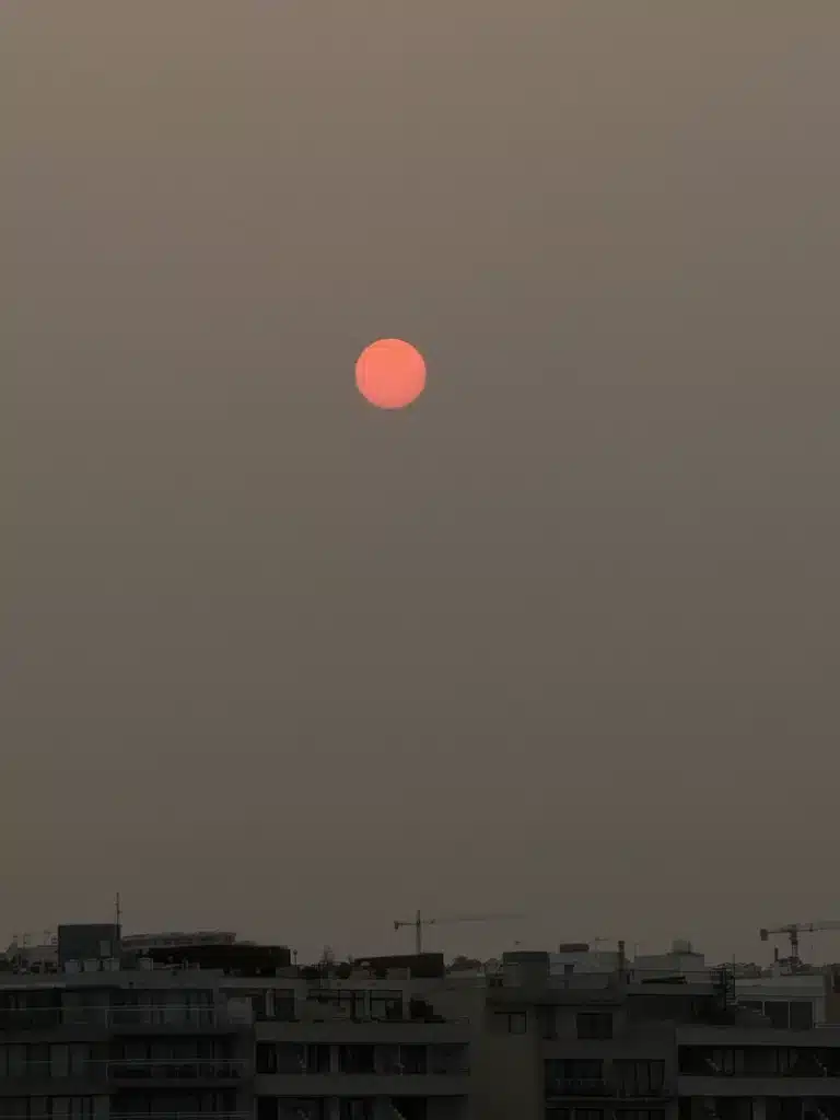 Scorpio Season image with a red sun over a quiet city skyline, symbolizing autumn light, balance, transition, and the reflective energy of this astrological season.