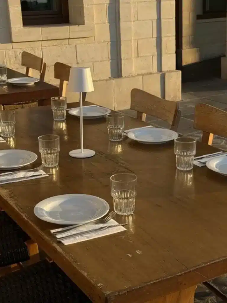 Scorpio Season image with a warmly lit table set with plates, glasses, and a small lamp, symbolizing harmony, gathering, beauty, and the deep energy of this astrological season.