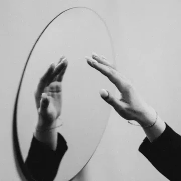 aries rising representation in black and white, hands reaching toward a mirror symbolizing the Ascendant as the first perception of the self