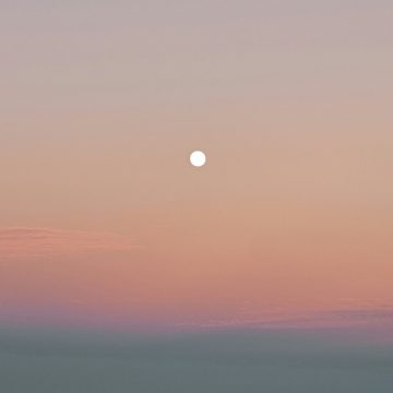 The Gemini Full Moon glowing in a pastel sky at dusk, against soft shades of peach, pink, and blue.