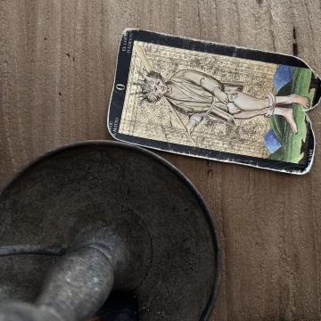 Vintage Fool tarot card from the Visconti Sforza deck on a wooden surface.