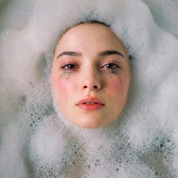Black Moon Lilith in Cancer, emotional portrait of a woman floating in a bubble bath, symbolizing vulnerability and care.