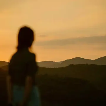 Mars enters Leo, represented by a silhouetted figure standing before a fiery golden sunset and distant hills.