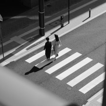 Neptune in the 2nd House, two people walking across a sunlit crosswalk in black and white, symbolizing fluid values, shifting material paths, and uncertainty around stability.