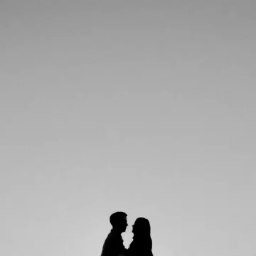 Rising sign compatibility represented by the silhouettes of two people facing each other beneath a vast grey sky.