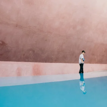 sagittarius rising street photography with a person walking across a blue pavement and pink wall background, vibrant movement and playful expansive atmosphere