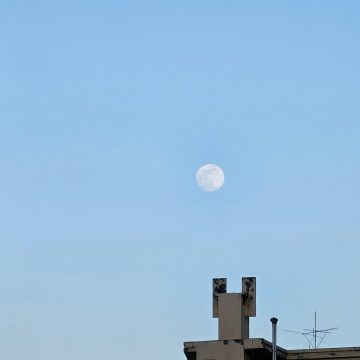 Venus in Virgo symbolized by the Moon rising in a clear blue sky above city buildings.